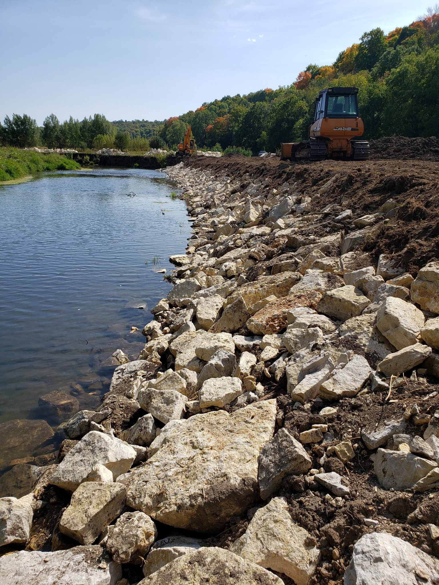 After: Stabilized riverbank with stone riprap reinforcement and proper grading